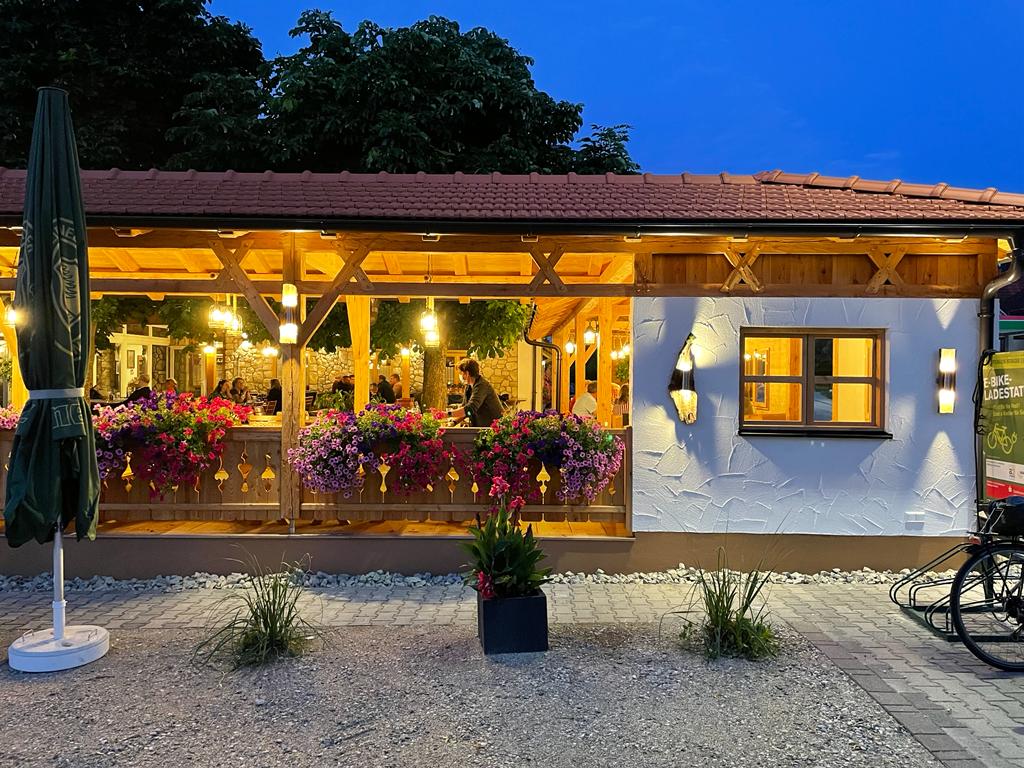 Ein drittes Bild vom Biergarten aussen. Diesmal Nachts, mit wunderschöner Beleuchtung und freier Sicht auf den belebten Betrieb im Biergarten.