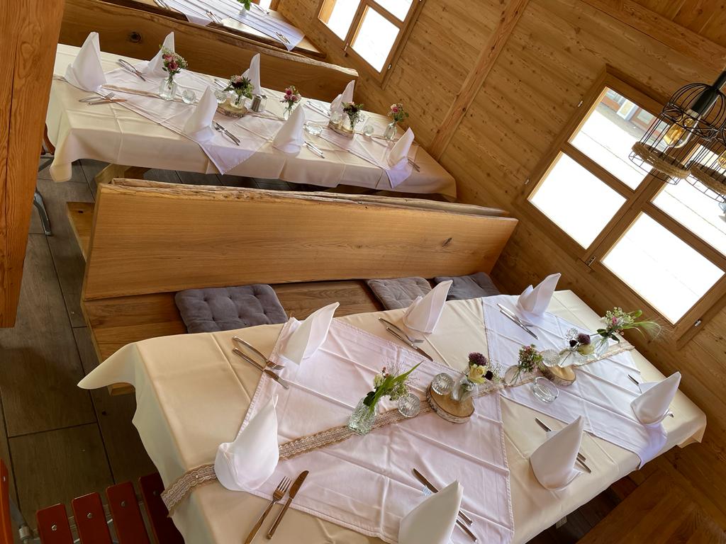 Bild zeigt einen weiß gedeckten Tisch mit Holzbänken im Biergarten, der Biergarten ist im Hüttenstil gebaut.